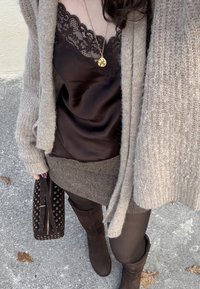 Brown satin camisole with lace trim, layered under a beige knitted cardigan. Brown herringbone-patterned skirt, dark tights, and tall brown boots.
