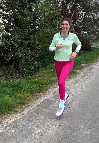 Conjunto deportivo que incluye una chaqueta de cierre ligero de color verde claro y leggings de color rosa brillante, con calcetines blancos y zapatillas de correr coloridas. Entorno al aire libre.