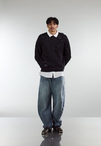 Black jumper with distressed texture, light grey collared shirt, loose blue jeans, and dark shoes. Minimalist design, no patterns or logos.