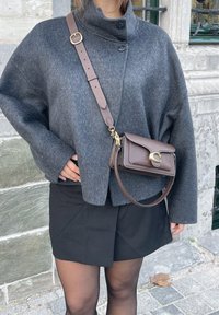 Chaqueta grande de mezcla de lana gris con cuello alto y botones negros, combinada con un bolso cruzado marrón con un cierre curvado.