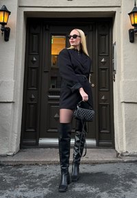 Mustast bleiserkleidist koosnev vööga kleit, läbipaistvad mustad sukkpüksid, põlveni ulatuvad mustad saapad ja tikandiga must käekott. Matte tekstuurid ja sujuv disain.