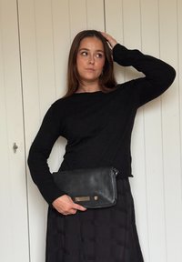 Mustast pika varrukaga kampsunist koosnev komplekt, mida kantakse volditud musta seelikuga, käes mustast nahast klapp, millel on kuldsed detailid ja tõmbluku kinnitusega.