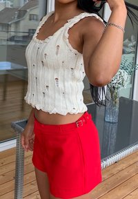 Débardeur tricoté blanc cassé avec des découpes et des bretelles tressées, associé à un short ajusté rouge vif avec une boucle sur le côté.