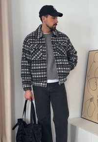 Blusão de lã aos quadrados em preto e branco, camisola cinza, jeans pretos e uma sacola preta. Padrão xadrez distinto, design com gola e fecho de correr.