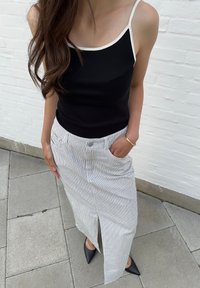 Μαύρο αμάνικο μπλουζάκι με λευκή περιμετρική ρίγα, συνδυασμένο με μακριά ριγέ φούστα με άνοιγμα στο πλάι και μαύρες μυτερές μπαλαρίνες. Αντίκτυπος από ασημένιο βραχιόλι.