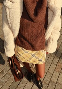 Pruun kootud kampsun kaelusega, kreemjas karvase sisuga mantel, kollane ruuduline miniseelik ja mustad mokassiinid. Pruun tekstuuriga käekott.