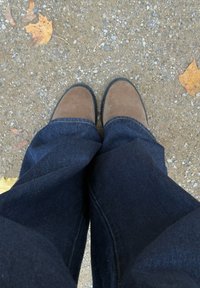 Pruunid seemisnahast saapad ümarate ninadega, kantud siniste teksadega, seisavad kruusapinnal, kus on laialt laotatud lehti.