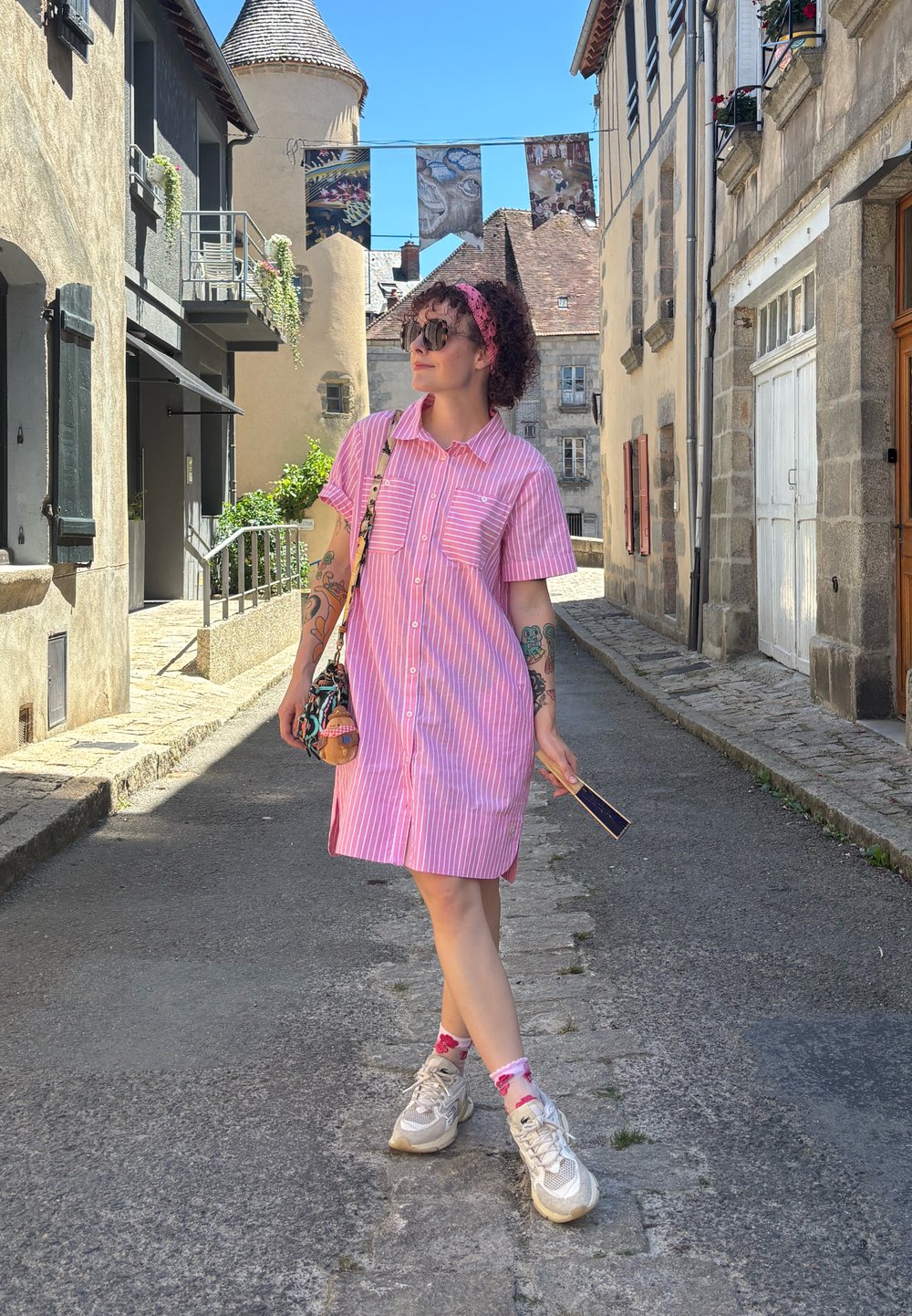 Vestido de botão em rosa e branco com riscas, de mangas curtas e dois bolsos no peito. Combinado com ténis cinzentos e meias estampadas. Saco de acessórios.