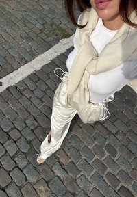 Cremfarbene, lockere Satin-Hosen mit Zugdetails, kombiniert mit einem weißen, figurschmeichelnden Langarmtop und einem weichen beige Schal.