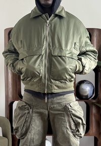 Veste bomber verte avec fermeture éclair à l'avant, grandes poches poitrine et poignets côtelés. Assortie à un pantalon cargo avec poches zippées.