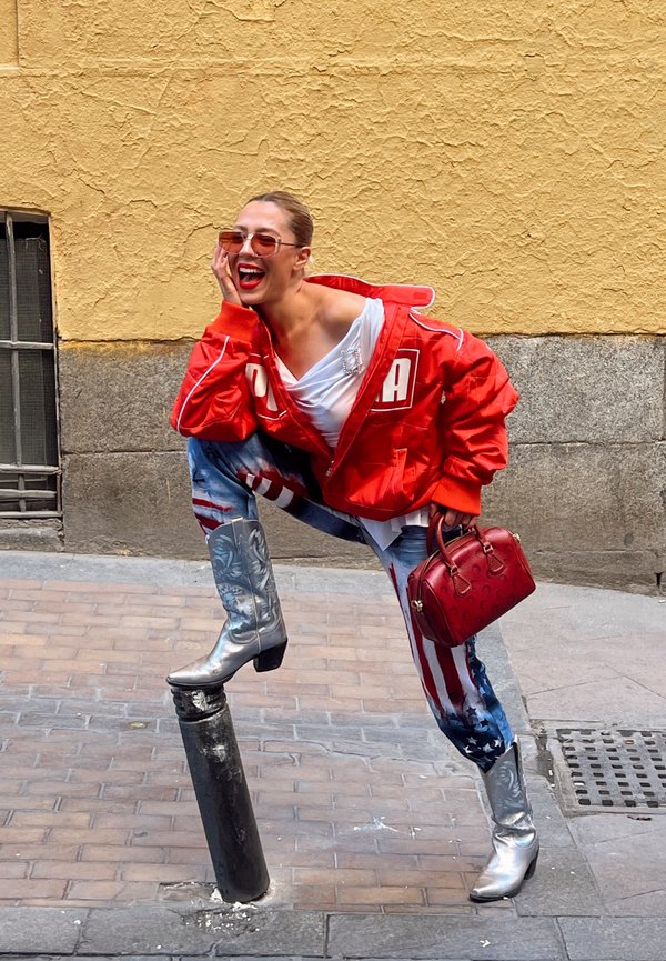 Veste surdimensionnée rouge avec des lettres blanches, haut blanc, jeans bleus avec des rayures rouges et blanches, bottes de cowboy argentées et un sac à main rouge.