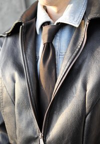 Must must jacket hõbedase tõmblukkuga, seljas helesinine denimpusa, mille kaela on seotud must siiditeks.