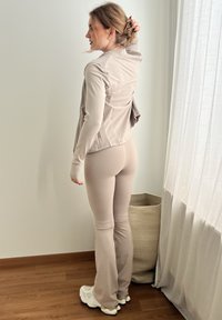 Veste beige clair et leggings assortis ajustés en tissu extensible. La veste est dotée d’un détail zippé, tandis que les leggings ont un ourlet évasé.