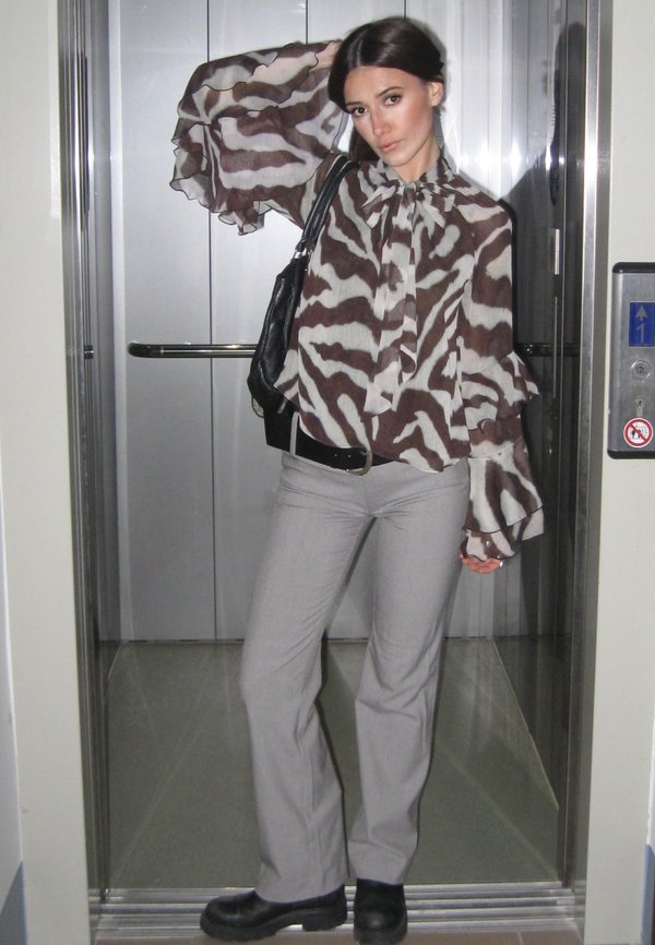 Blusa de estampado de cebra marrón y beige con mangas con volantes, combinada con pantalones gris claro y botas negras gruesas, situada en un ascensor.