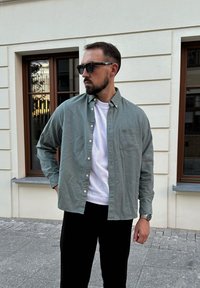 Šviesiai žalia marškinėlių švarkelis ant baltos marškinėlių, derinamas su juodomis kelnėmis. Papuoštas kairėje krūtinės pusėje esančia kišenėle ir dėvimas su saulės akiniais.