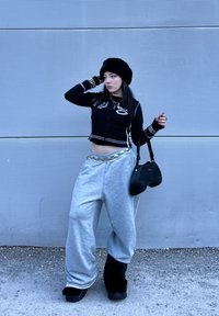 Pull noir raccourci avec détails blancs, pantalon de survêtement gris surdimensionné, chapeau en fourrure et sac à main noir ; accessoires comprenant bracelets et chaînes.