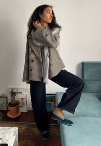 Brun og kremrutete dobbeltrad blazer, grått skjerf, mørk denim bukser, blå loafers, kontrasterende teksturer og avslappet passform.