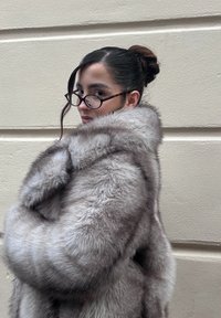 Kabát z umelého kožušina svetlo šedej farby s jemnou textúrou, širokým golierom a spustenými ramenami, nosený cez čierne tričko.