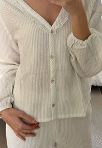 Set de pijamale cu textură de culoare crem, compus dintr-o bluză căptușită cu guler volant și mâneci lungi, asociată cu pantaloni asortați.