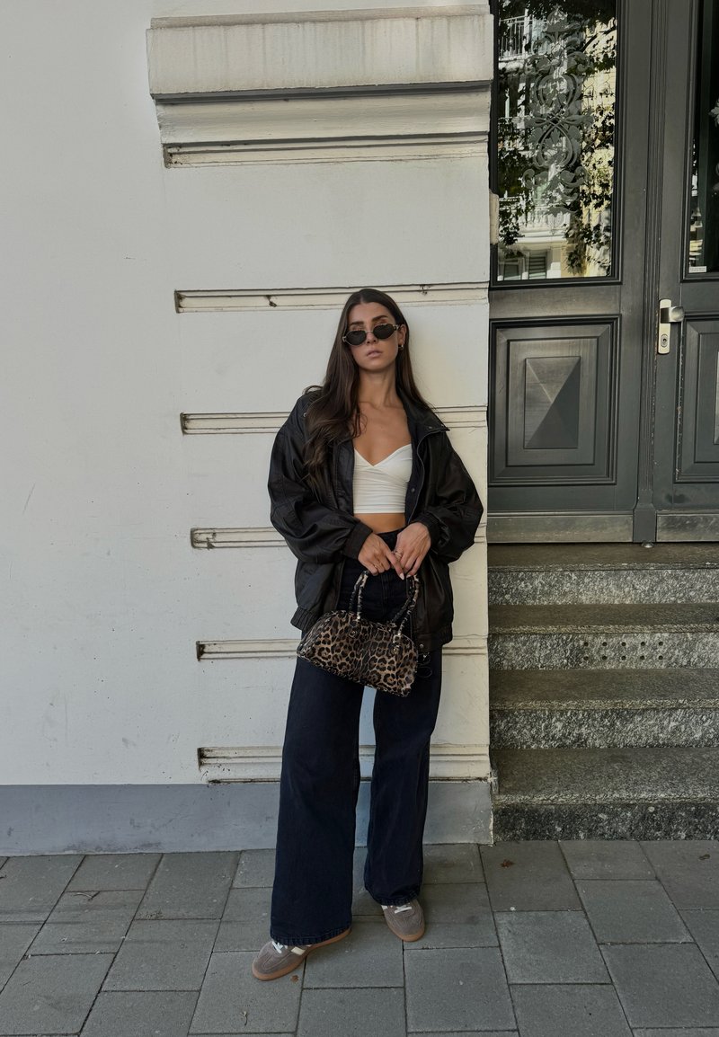 Μαύρο oversized μπουφάν, λευκό crop top, σκούρο παντελόνι με φαρδιά κοπή και τσάντα με λεοπάρ σχέδιο. Τα αξεσουάρ περιλαμβάνουν σκούρα στρογγυλά γυαλιά ηλίου.