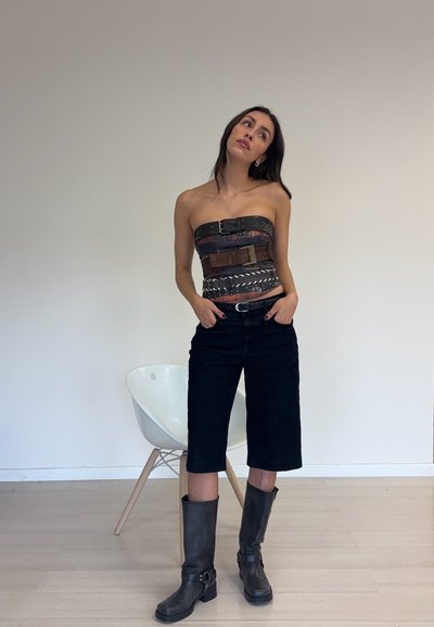 Top sin tirantes con cinturones marrones y negros con hebillas, combinado con pantalones cortos negros hasta la rodilla y botas negras hasta la rodilla.