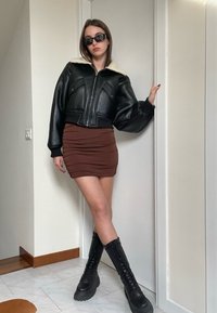 Svart läder cropped jacka med fårskinnskrage, kombinerad med en brun rynkad minikjol och knähöga svarta snörstövlar.