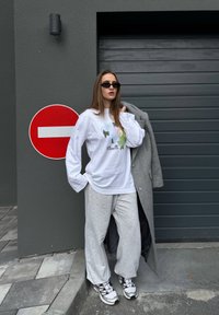 White long-sleeve shirt with colorful print, gray sweatpants, and a gray coat, paired with black sunglasses and white sneakers. Red no-entry sign in background.