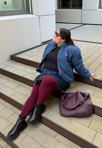 Chaqueta de mezclilla tipo puffa con cremalleras, top negro, mini falda de mezclilla deshilachada, leggings burdeos, botines negros y un bolso burdeos.