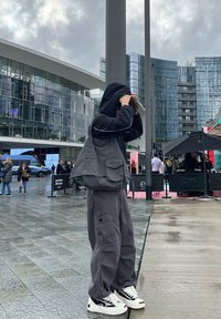 Haut à capuche surdimensionné gris et pantalons baggy assortis avec poches, associés à des baskets blanches avec des accents noirs. Cadre urbain en plein air.