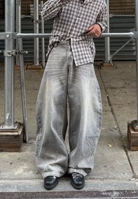 Laza, szürke farmernadrág fakó mosással és kopott hatással, kockás szürke inggel és fekete cipővel párosítva.