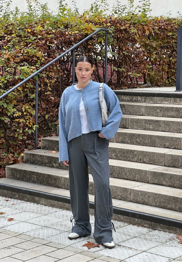 Light blue cropped cardigan over a white top and gray wide-leg trousers. Features a button closure and light-colored shoes. Potentially a handbag.