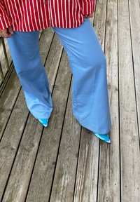 Pantaloni a gamba larga azzurri abbinati a tacchi a spillo blu e bianchi a motivo vivace, completati da una camicia a righe rosso e bianco.