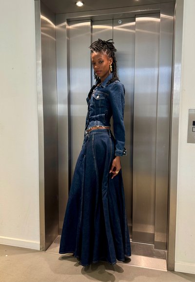 Conjunto de denim que incluye una chaqueta corta y una falda larga, ambos en azul oscuro. La falda tiene un diseño acampanado y la chaqueta incluye herrajes plateados.