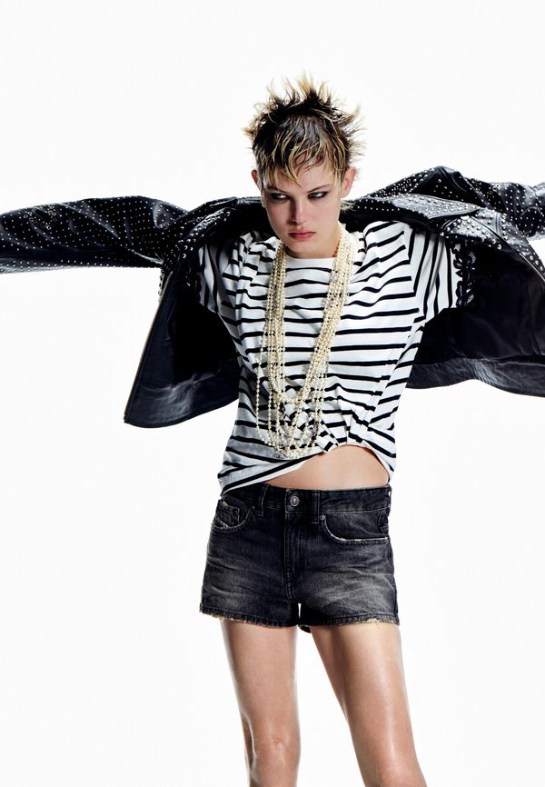Chaqueta negra con tachuelas, camisa blanca y negra a rayas anudada en la cintura, pantalones cortos de mezclilla oscura desgastados, collares de perlas en capas.