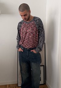Hosszú ujjú kötött póló piros és szürke mintákkal, magas derekú kék farmernadrággal párosítva, amely laza szabású és elülső zsebekkel rendelkezik.