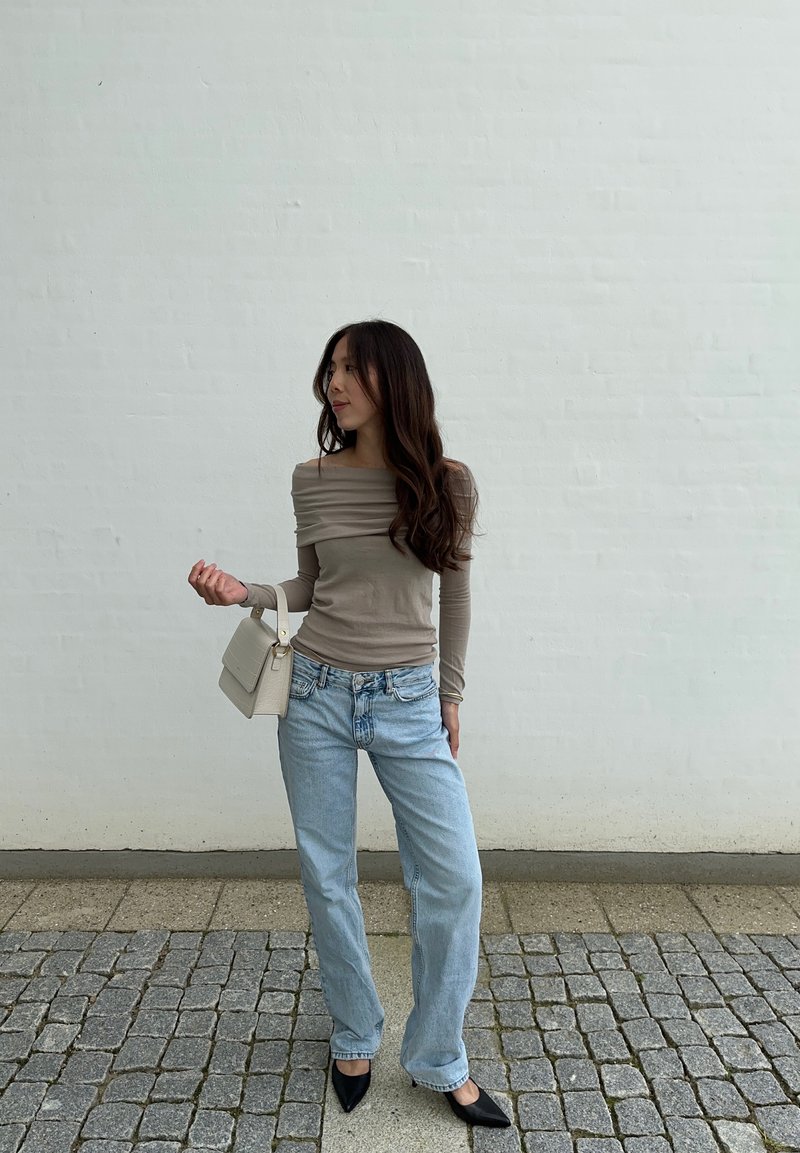 Μπεζ μπλούζα με μακριά μανίκια και  gathered λεπτομέρεια, ανοιχτό μπλε παντελόνι κατευθείαν πόδι, και μαύρες μυτερές παπούτσες. Κρατάει μια μικρή λευκή τσάντα.