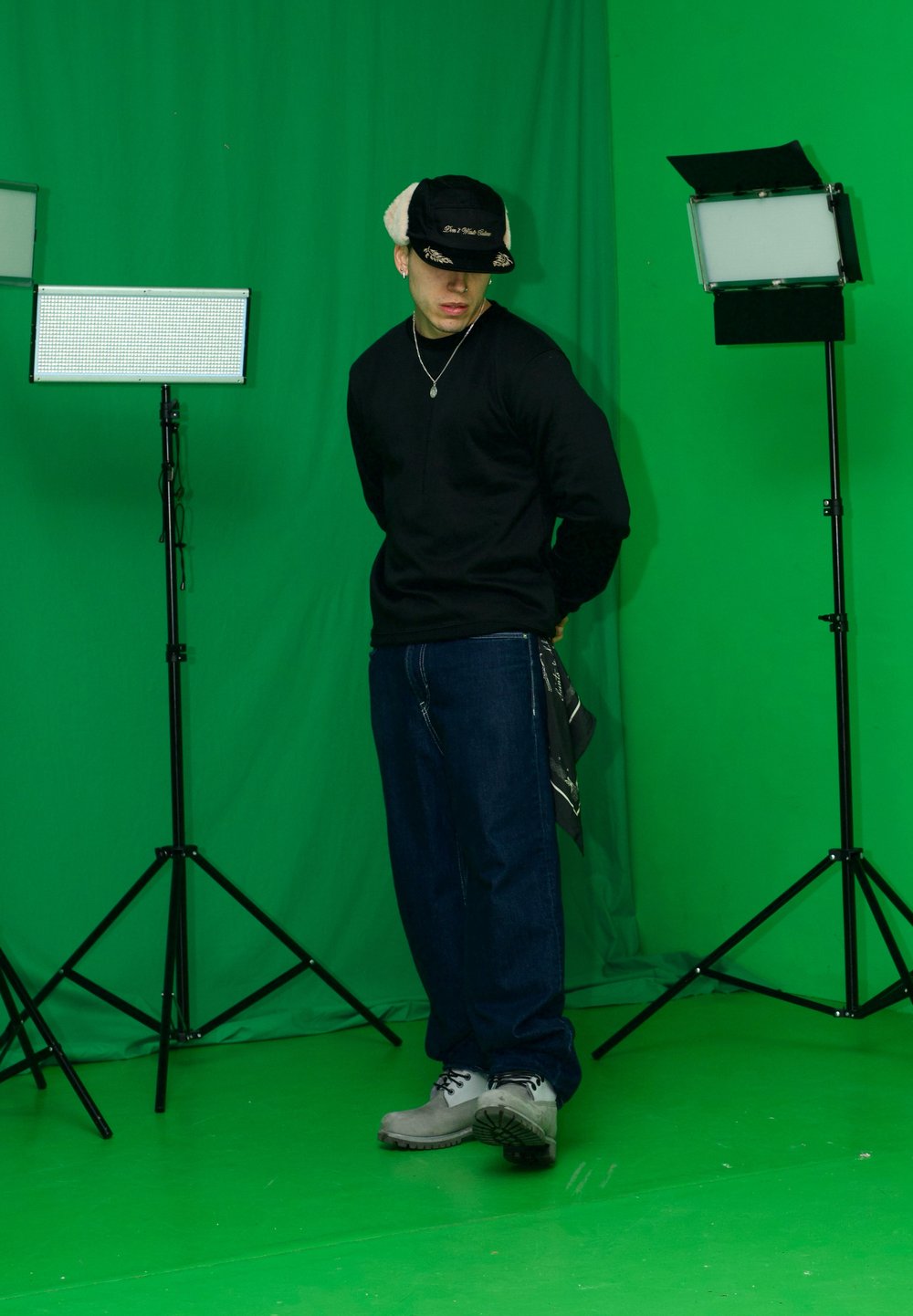 Must pikkade varrukatega särk, tumedad sinised teksad, hallid kingad; peas must ja beež müts; stuudio tuled statiivil; roheline taust.