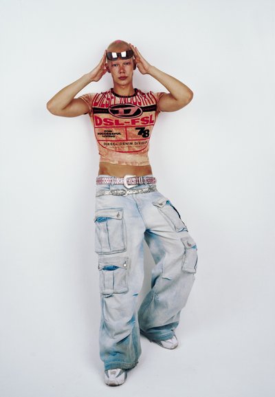 Modelo que lleva una camiseta gráfica ajustada de color naranja con texto negro, combinada con pantalones cargo de color azul claro que cuentan con bolsillos y un cinturón plateado.