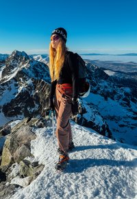 Buitensporter die klimt, gekleed in een zwart shirt met lange mouwen en een bruine broek, met een zwarte muts en zonnebril, uitgerust met een ijsbijl op een besneeuwde bergtop.
