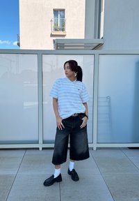Blå och vitrandig polo-tröja, svarta vida denim-culotter, vita strumpor och svarta plattformsskor. Står framför en glasbakgrund.