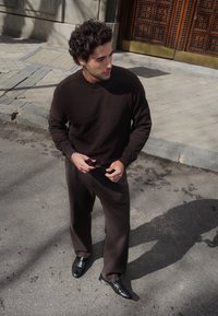 Rjava pletena jopica v kombinaciji z ujemajočimi rjavimi krojenimi hlačami. Obleka je dopolnjena z črnimi usnjenimi čevlji in sončnimi očali.