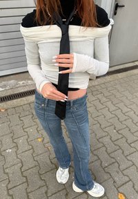 Top fără umeri din material alb-negru, cu panglică neagră, blugi albaștri evazați și adidași albi, pe fundal de paviment texturat.