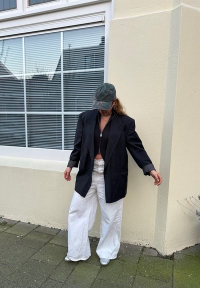 Blazer negro de doble botonadura, top negro corto, pantalones anchos blancos y una gorra de béisbol de camuflaje. Zapatos plateados que reflejan la luz.