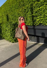 Lepardmønstret totebag, stoffmateriale, stor rektangulær form. Modell iført rød tettsittende topp og oransje bukser med sidestiper, solbriller.
