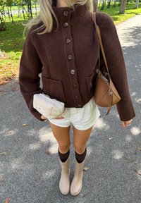 Ruda megzta kardiganas su aukštu apykakle ir mygtukų uždarymu, derinama su baltais šortais, rudomis iki kelių kojinėmis ir kreminėmis gumineis batais. Laikomas lengvas krepšys.