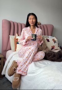 Ensemble de pyjama rose avec motifs de croissants et de cœurs, tissu doux, manches longues, et passepoil contrasté. Chaussons beiges à design ouvert.