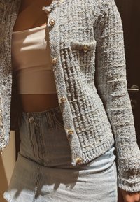 Blå texturerad cardigan med pärlknappar, vävd design, fransade kanter, tillsammans med en ljus topp och jeanskjol.