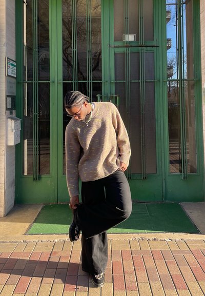 Suéter de punto en color beige con motas amarillas, combinado con pantalones negros holgados y zapatos con estampado, frente a puertas de entrada verdes.