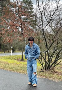 Giacca di jeans con hardware argento, jeans oversized blu chiaro con orlo sfilacciato, abbinati a calzature aperte e occhiali da sole.