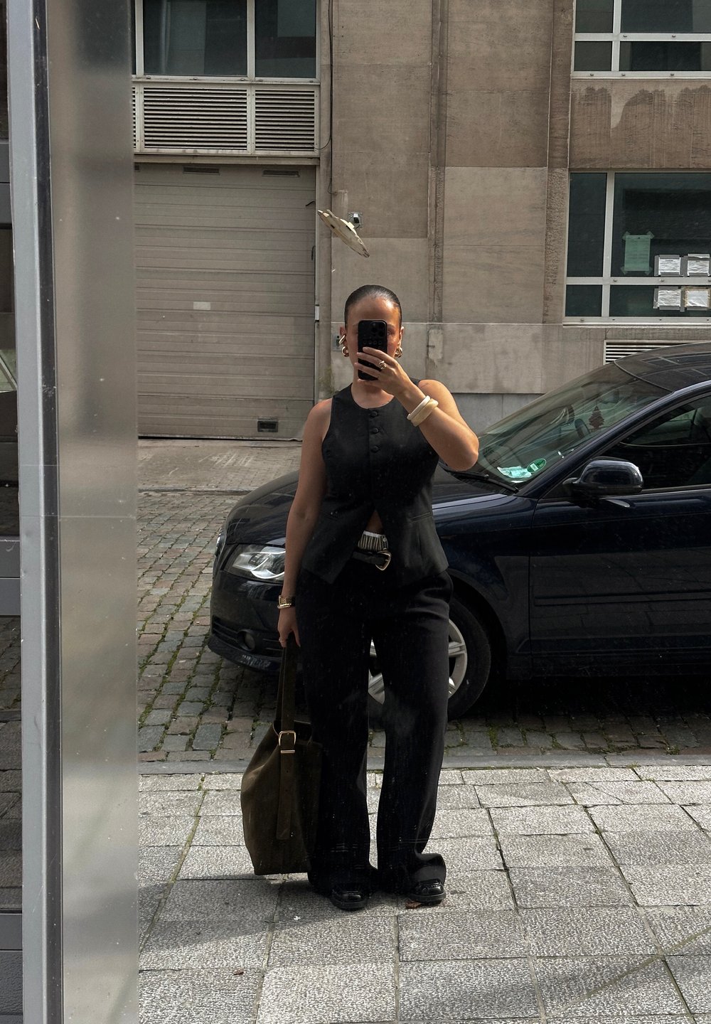 Μαύρο αμάνικο τοπ με κουμπιά, ψηλόμεσα μαύρα παντελόνια και μια σκούρα τσάντα tote. Υφασμάτινη επιφάνεια με λαμπερά αξεσουάρ κοσμημάτων.